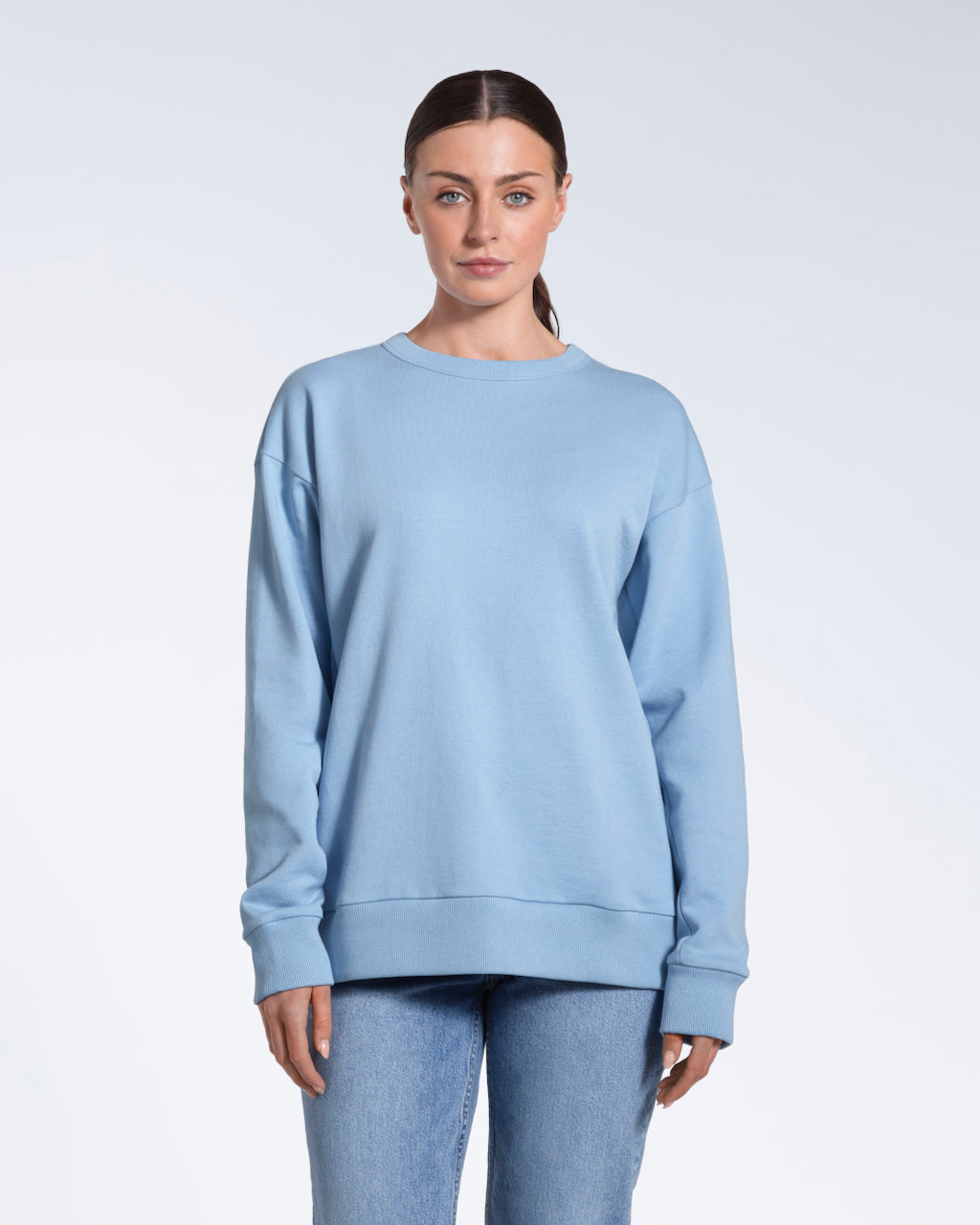 A woman looking into the camera with her arms by her side, modelling a plain blue oversized organic cotton sweatshirt.