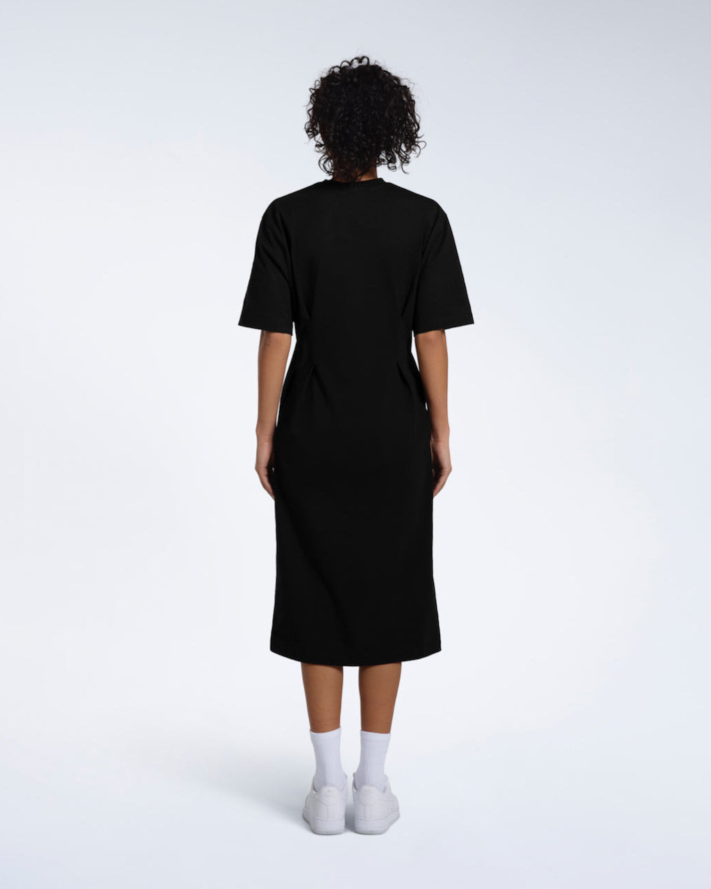 A women facing away from the camera, modelling a plain black, organic cotton midi t shirt dress.