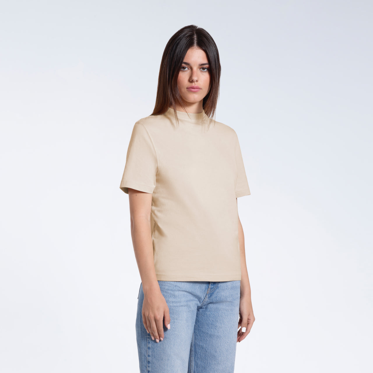 A woman looking into the camera with her arms by her sides, modelling a plain beige organic cotton t shirt.