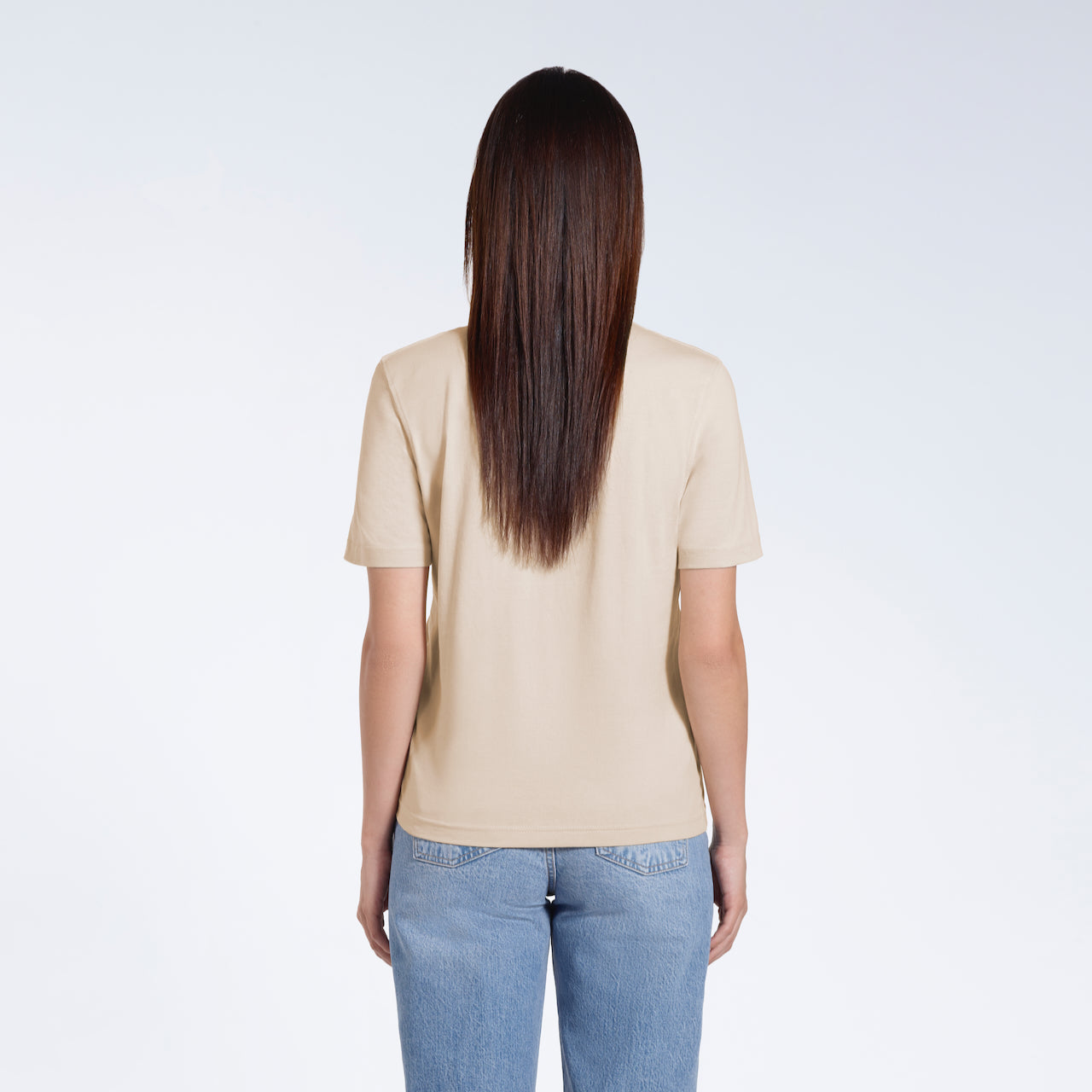 A woman with her back to the camera, modelling a plain beige short sleeve organic cotton t shirt.