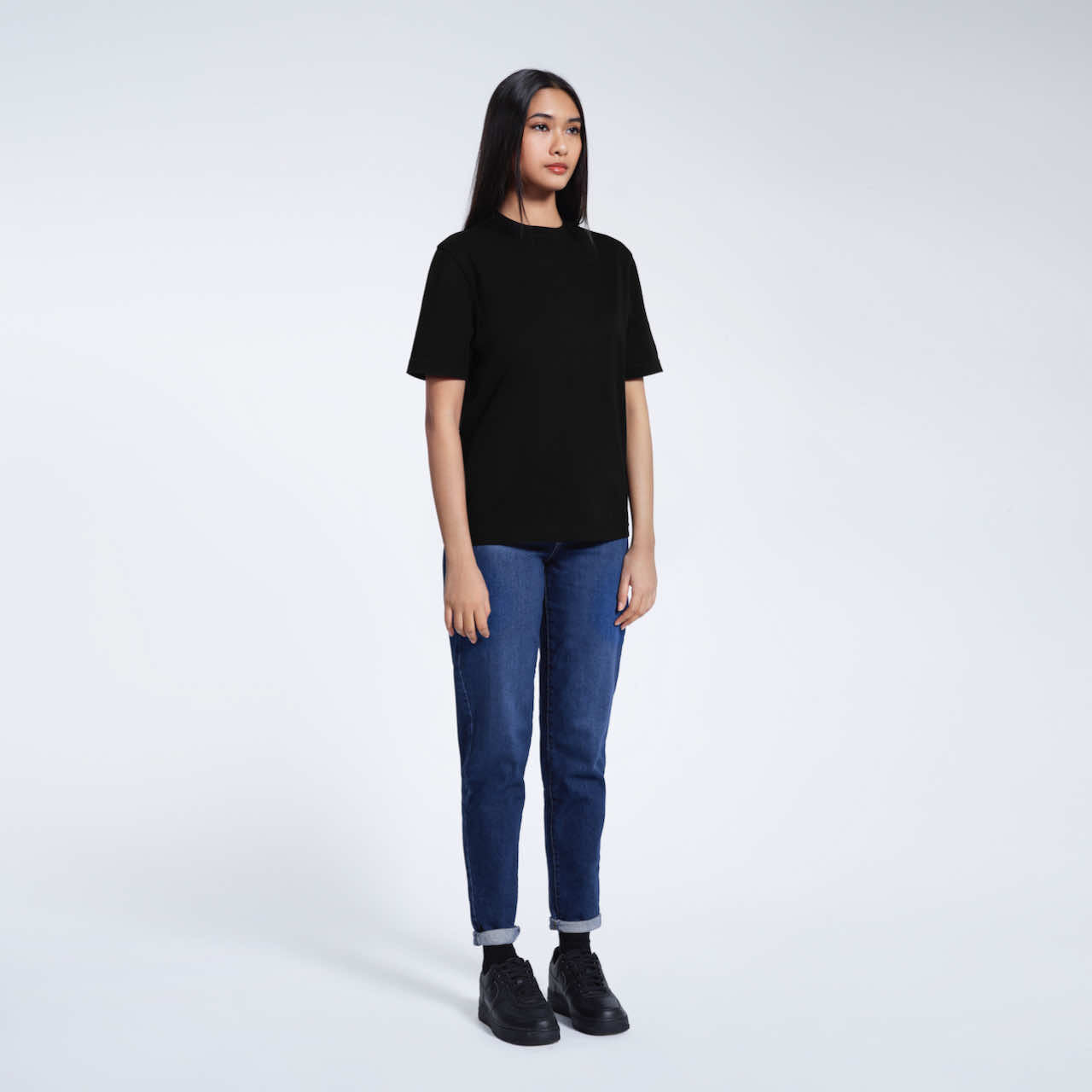 A full body photo of a woman with her arms at her sides, modelling a plain black short sleeve organic cotton t shirt.