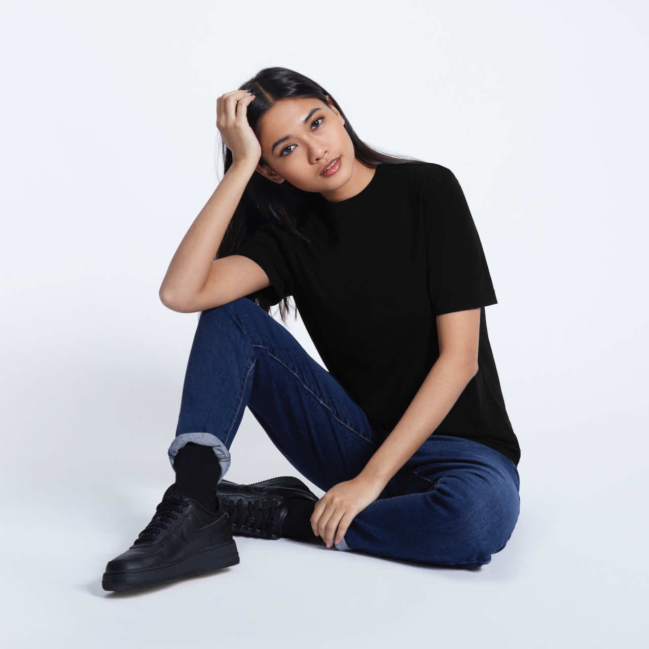 A woman sitting on the floor looking into the camera, modelling a plain black short sleeve organic cotton t shirt.