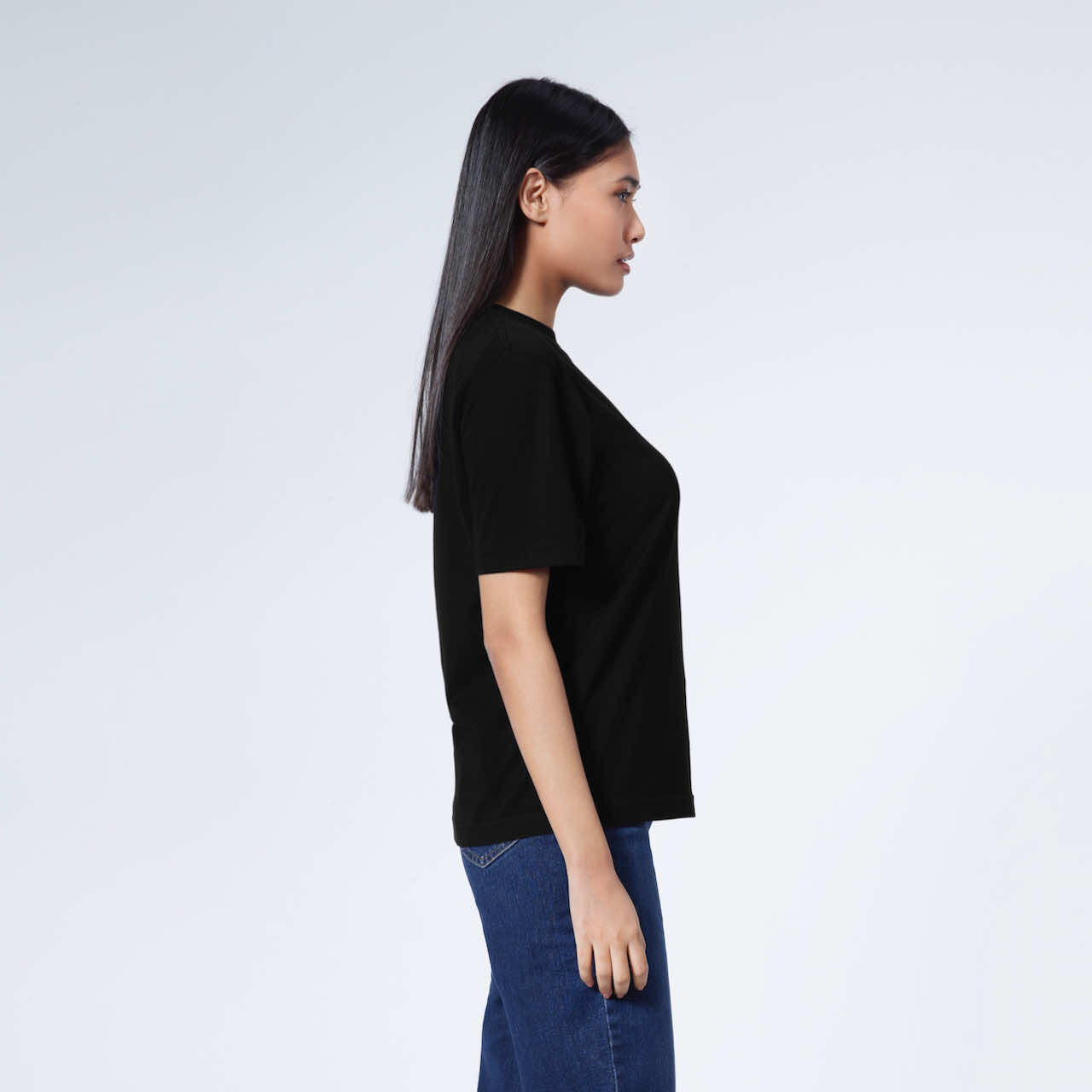 A woman facing side on, modelling a plain black short sleeve organic cotton t shirt.