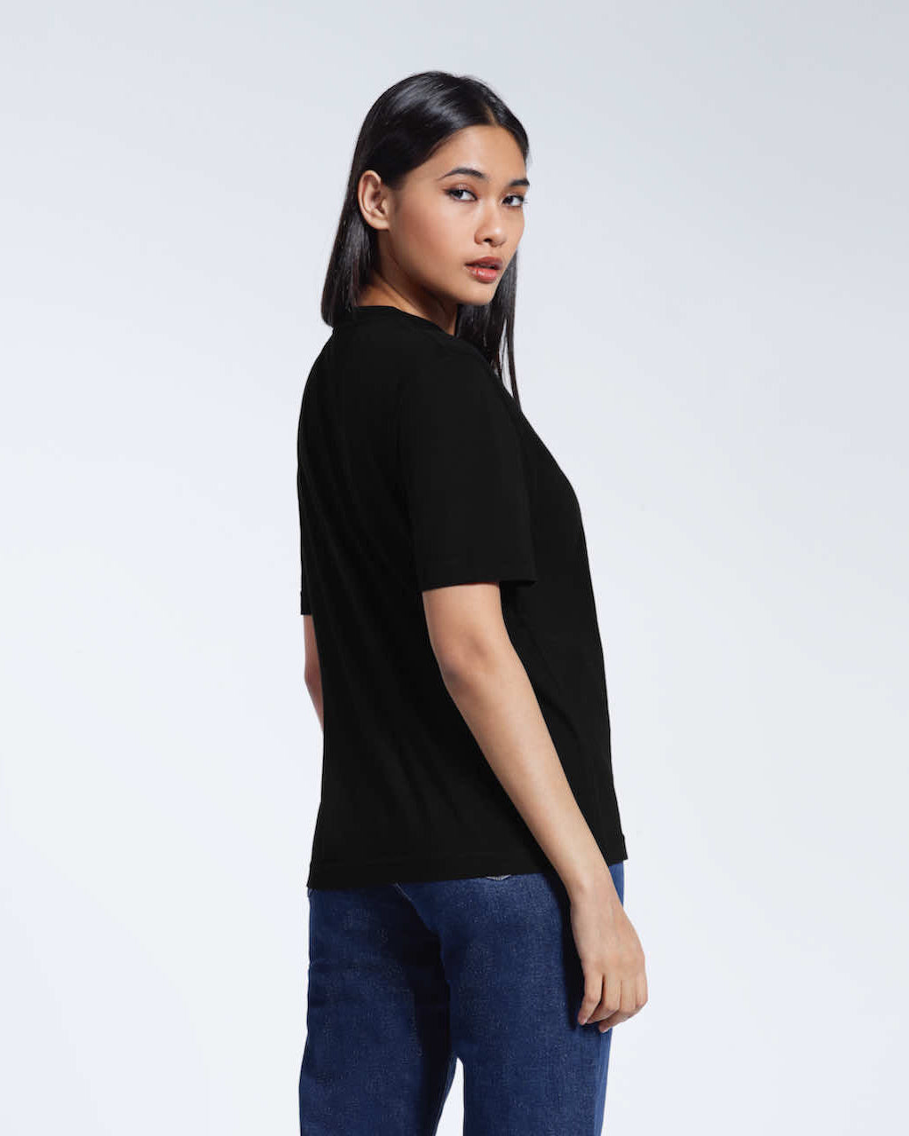 A woman looking back at the camera, modelling a plain black organic cotton t shirt.