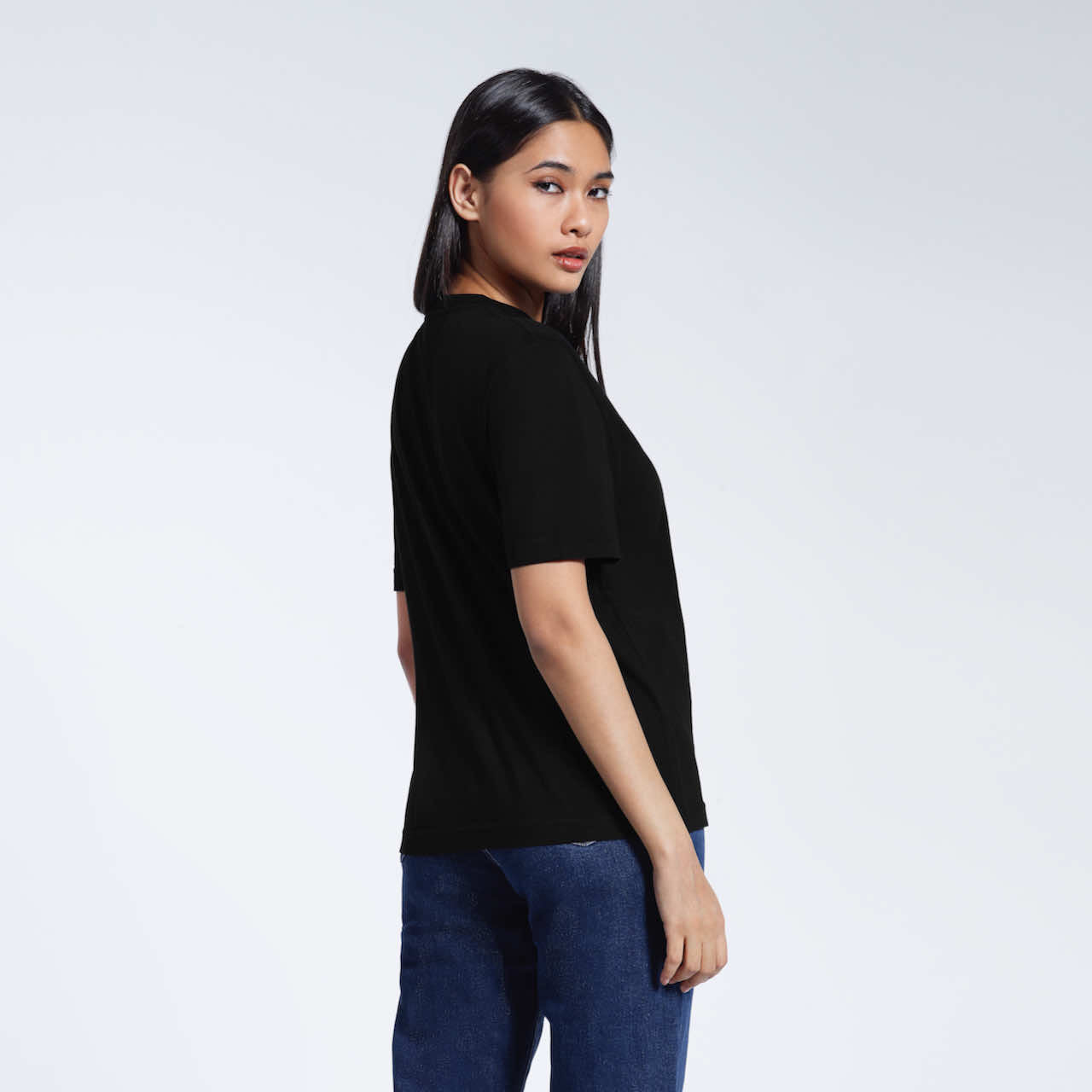 A woman looking back at the camera, modelling a plain black organic cotton t shirt.