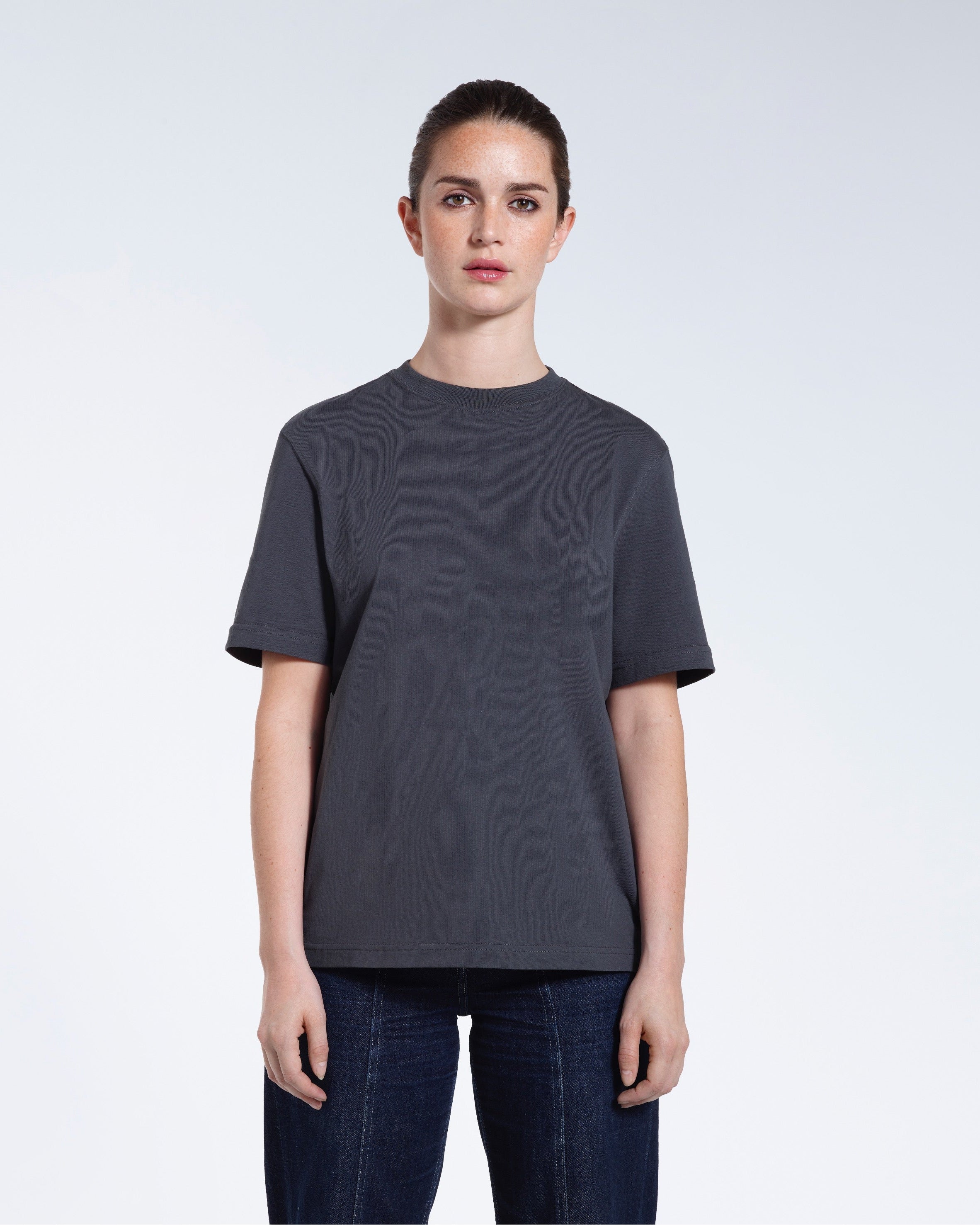 A woman facing front on looking at the camera, modelling a dark grey short sleeve organic cotton t shirt.