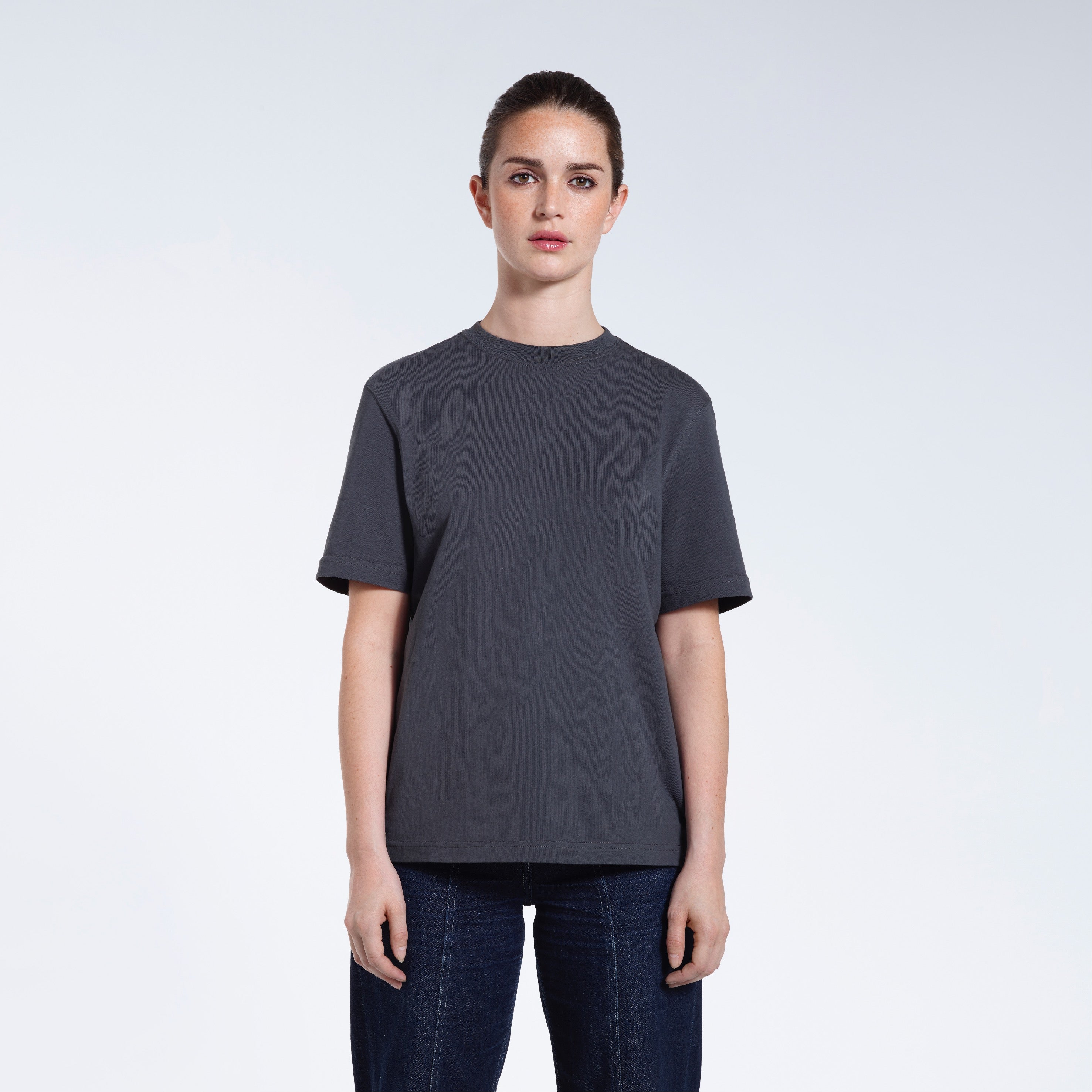 A woman facing front on looking at the camera, modelling a dark grey short sleeve organic cotton t shirt.