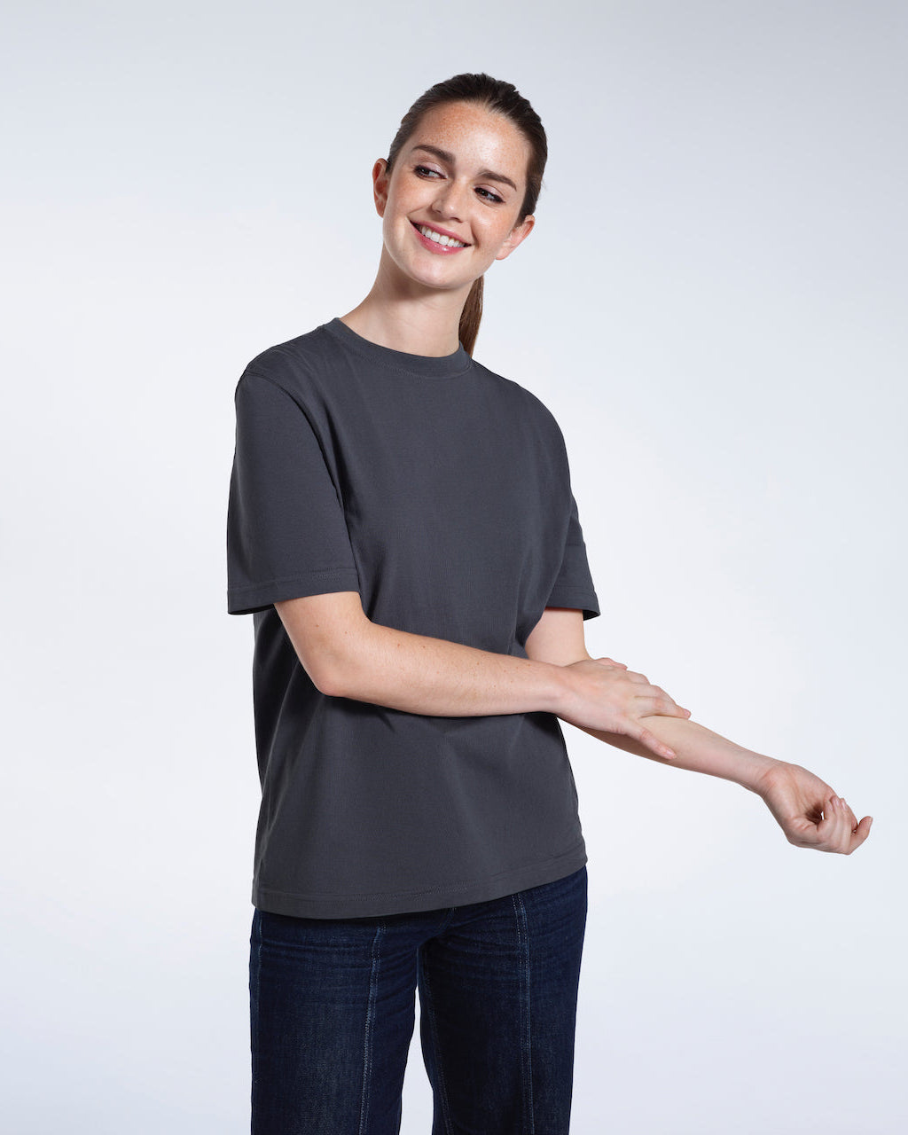 A woman smiling touching her arm, modelling a plain dark grey short sleeve organic cotton t shirt.