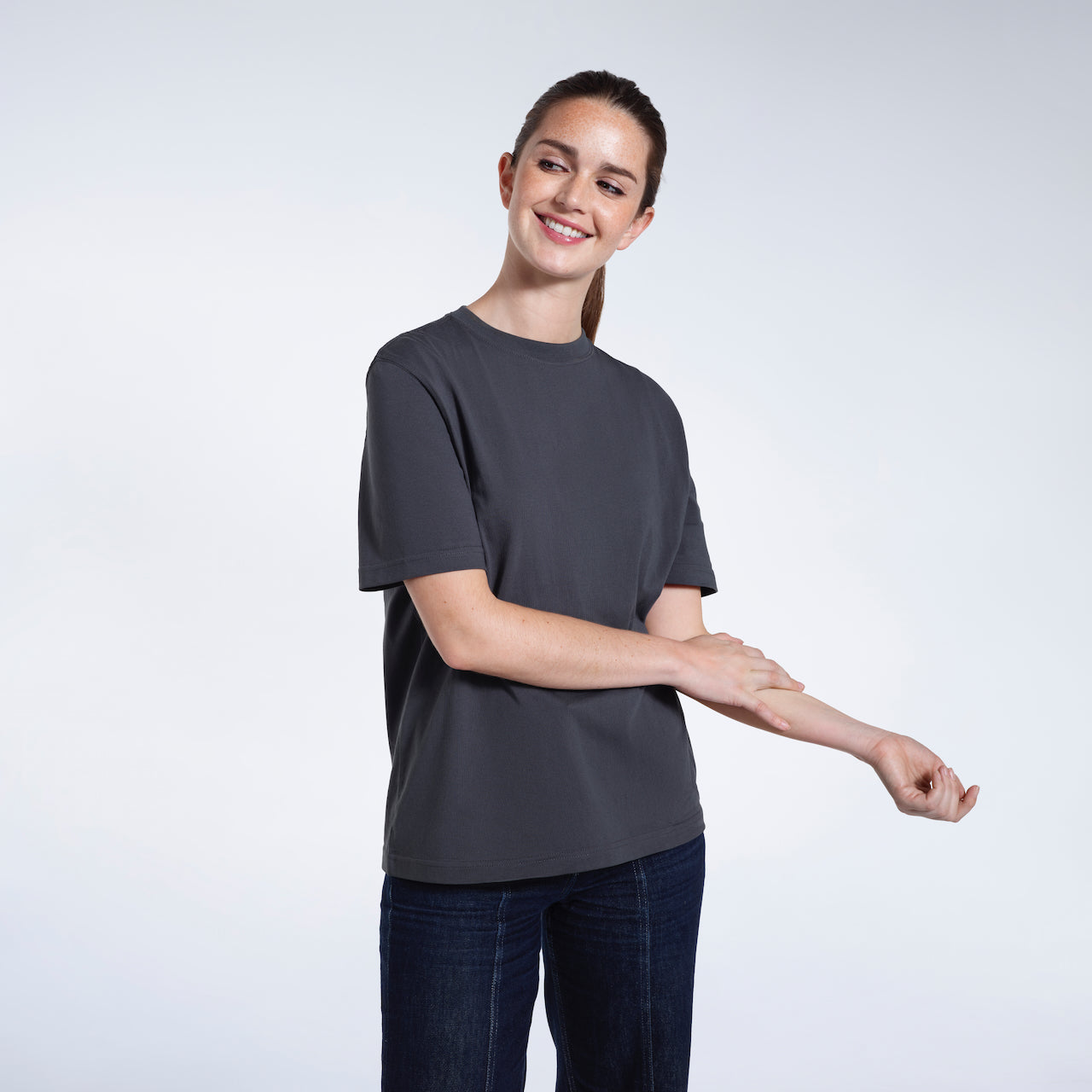 A woman smiling touching her arm, modelling a plain dark grey short sleeve organic cotton t shirt.