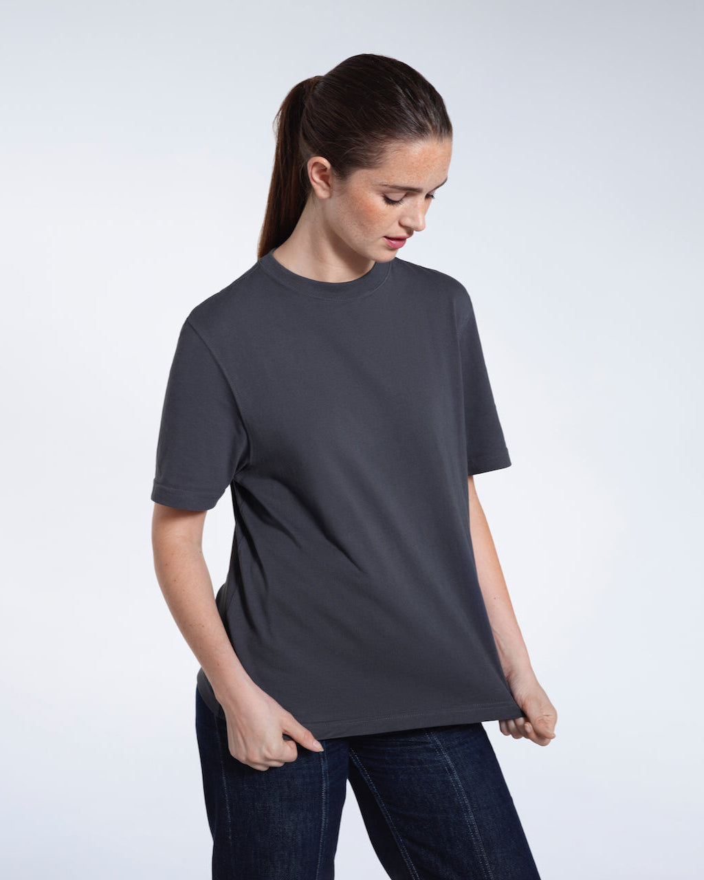 A woman ooking down and touching the bottom of her plain dark grey short sleeve organic cotton t shirt.