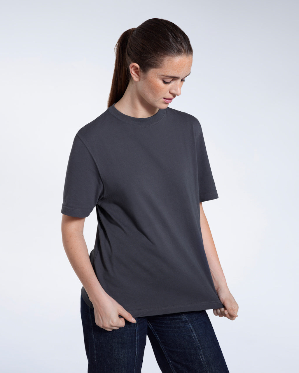 A woman looking down and touching the bottom of her plain dark grey short sleeve organic cotton t shirt.