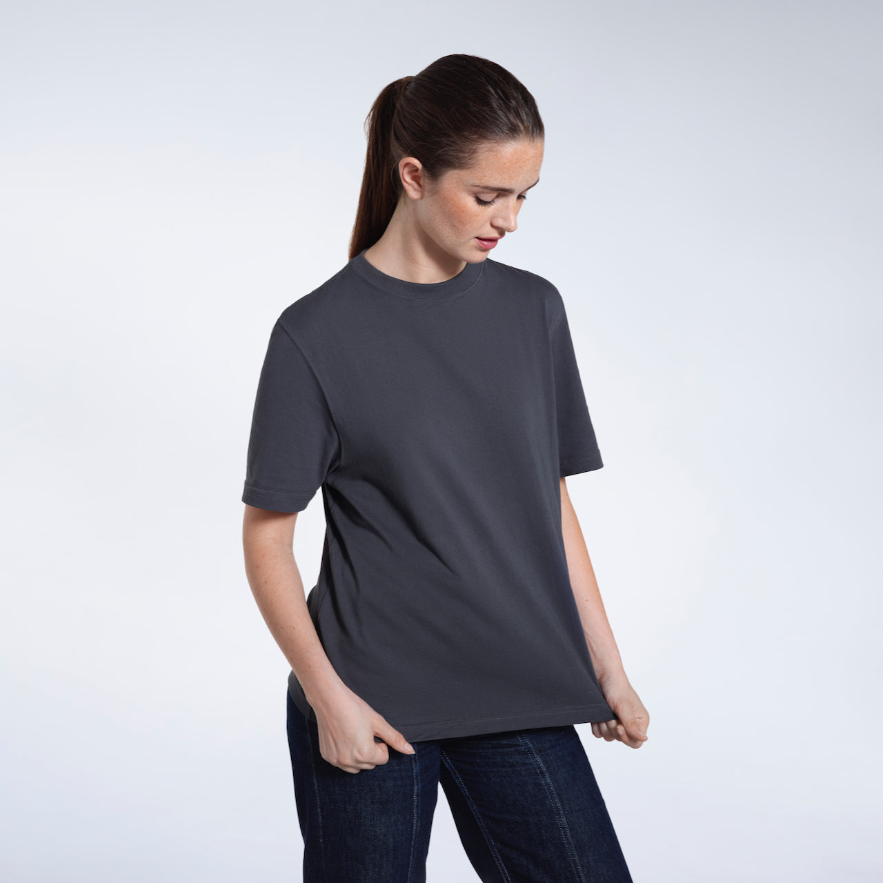 A woman ooking down and touching the bottom of her plain dark grey short sleeve organic cotton t shirt.