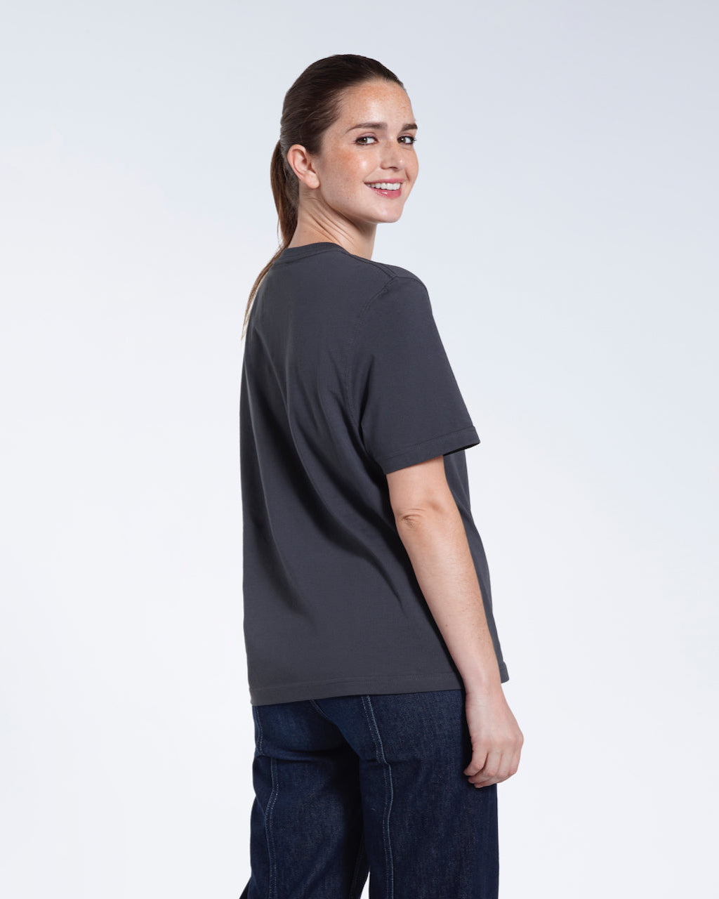 A woman turned towards the camera smiling, modelling a plain dark grey short sleeve organic cotton t shirt.