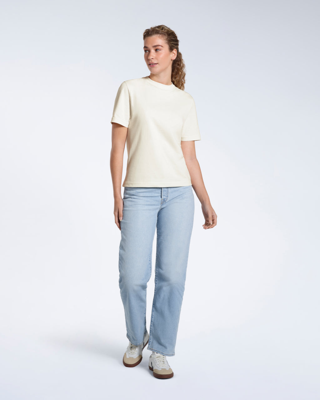A woman looking away from the camera, modelling an ecru short sleeve organic cotton t shirt.