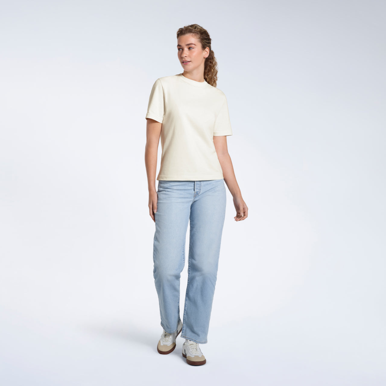 A woman looking away from the camera, modelling an ecru short sleeve organic cotton t shirt.