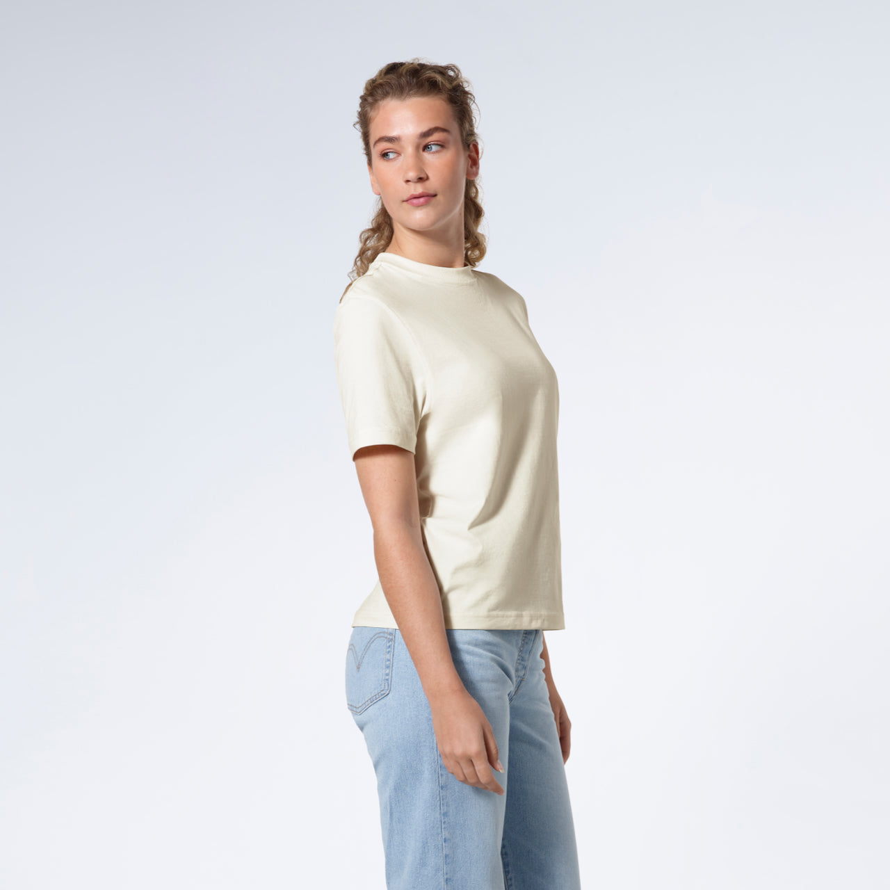 A woman facing side on looking back, modelling a plain ecru short sleeve organic cotton t shirt.