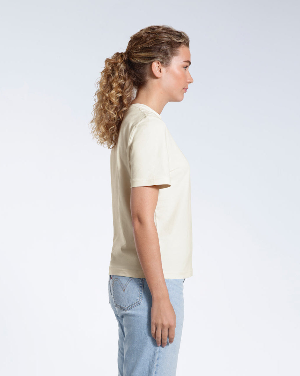 A woman facing side on, modelling a plain ecru short sleeve organic cotton t shirt.