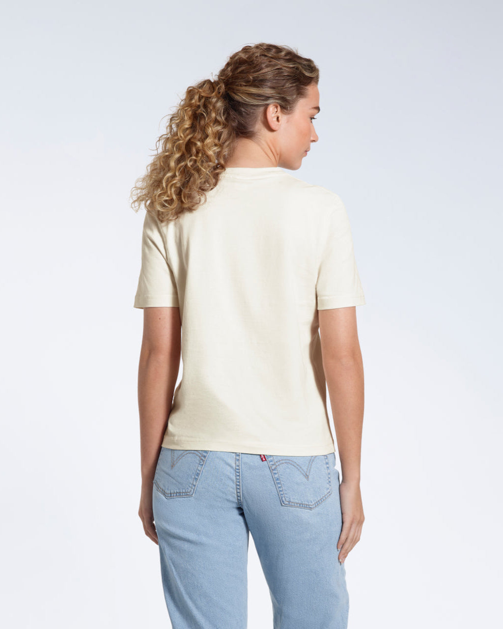 A woman with her back to the camera, modelling a plain ecru short sleeve organic cotton t shirt.