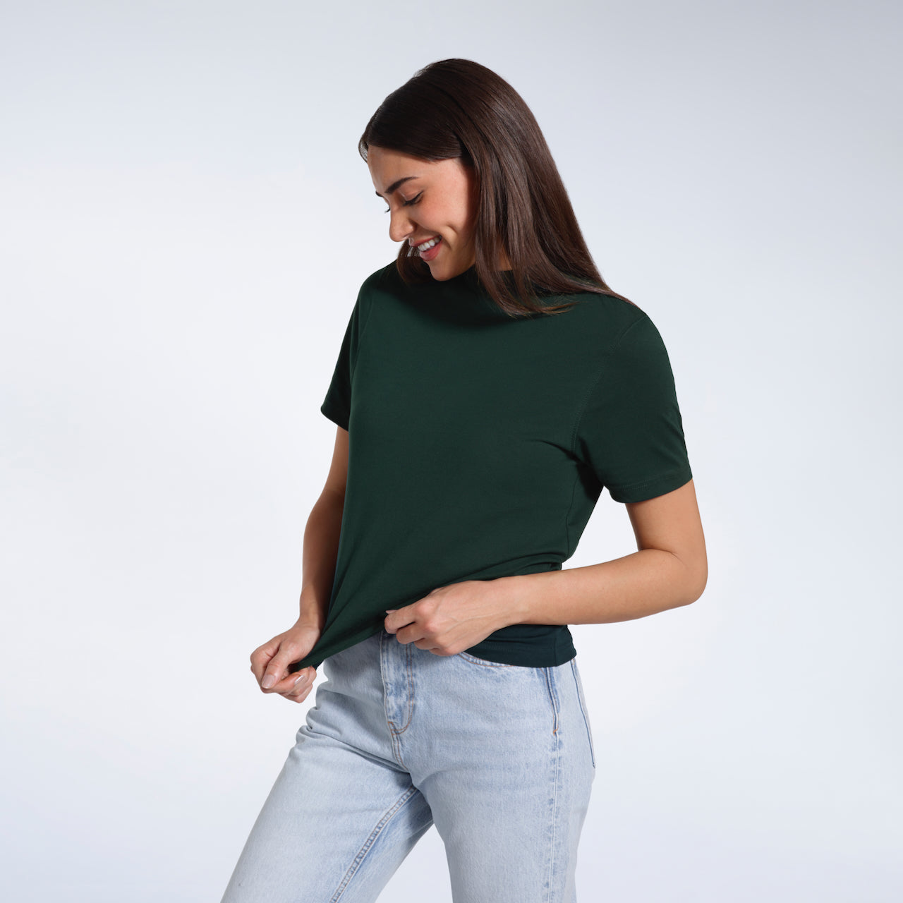 A woman looking down smiling and touching the bottom of her plain green short sleeve organic cotton t shirt.
