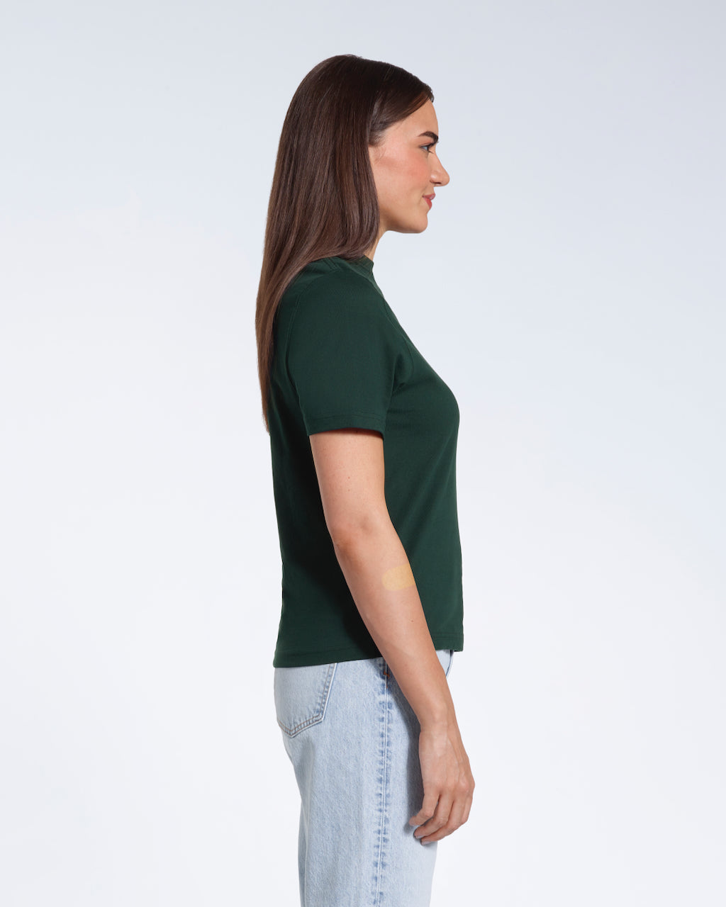A woman facing side on, modelling a plain green short sleeve organic cotton t shirt.