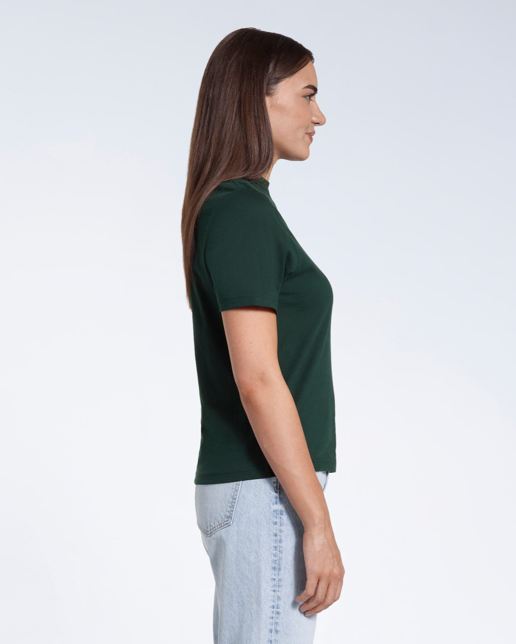 A woman facing side on, modelling a plain green short sleeve organic cotton t shirt.