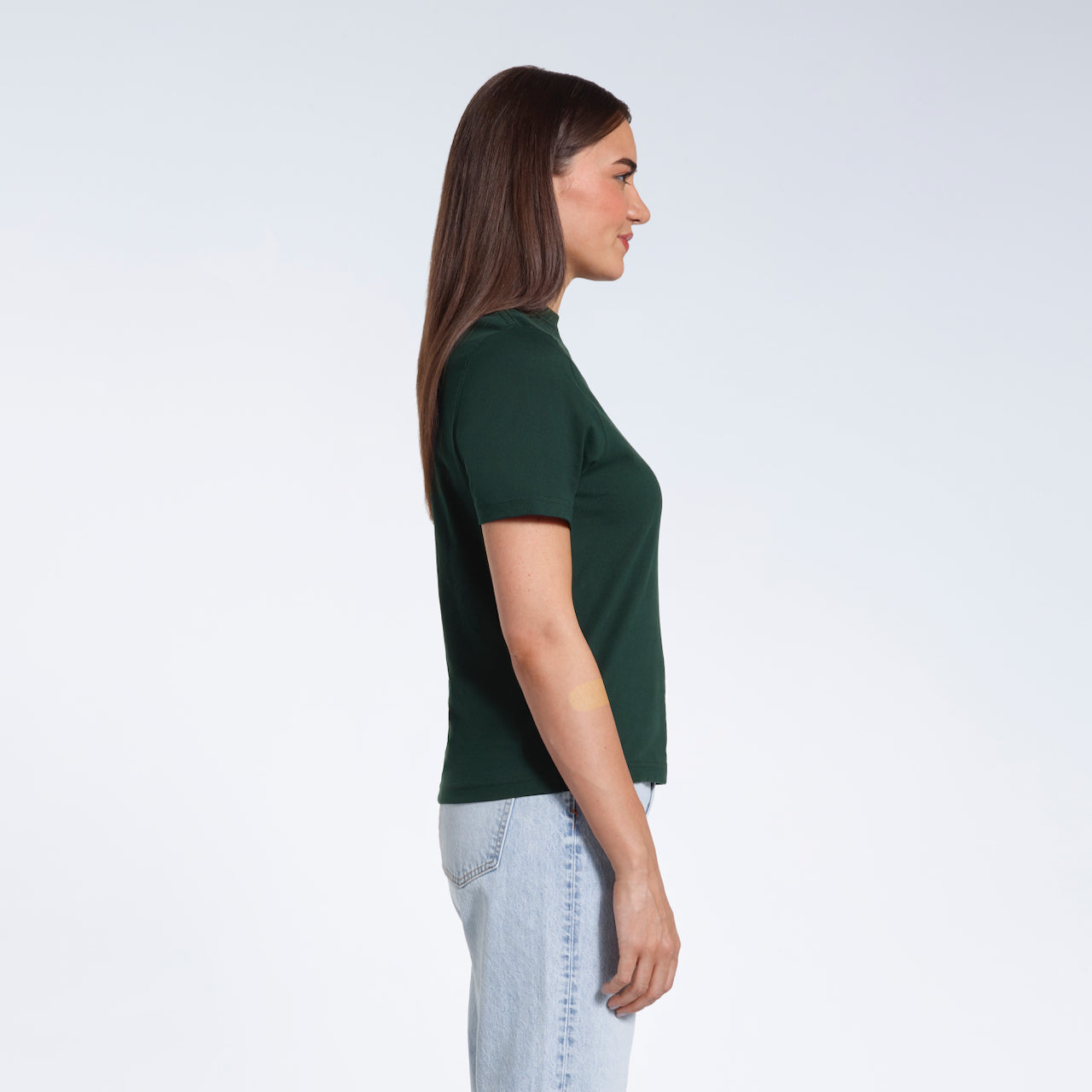 A woman facing side on, modelling a plain green short sleeve organic cotton t shirt.