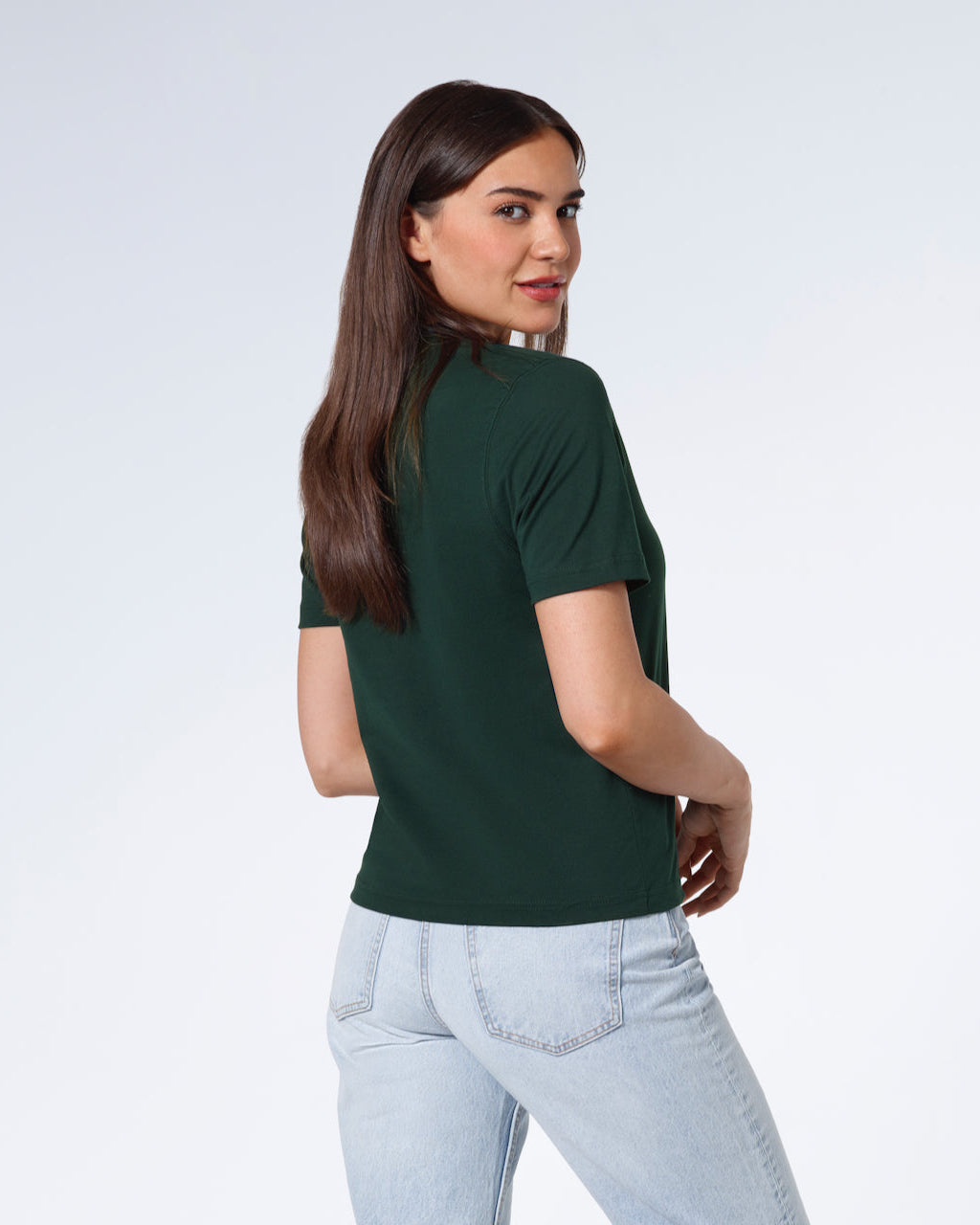 A woman turned towards the camera smiling, modelling a plain green short sleeve organic cotton t shirt.