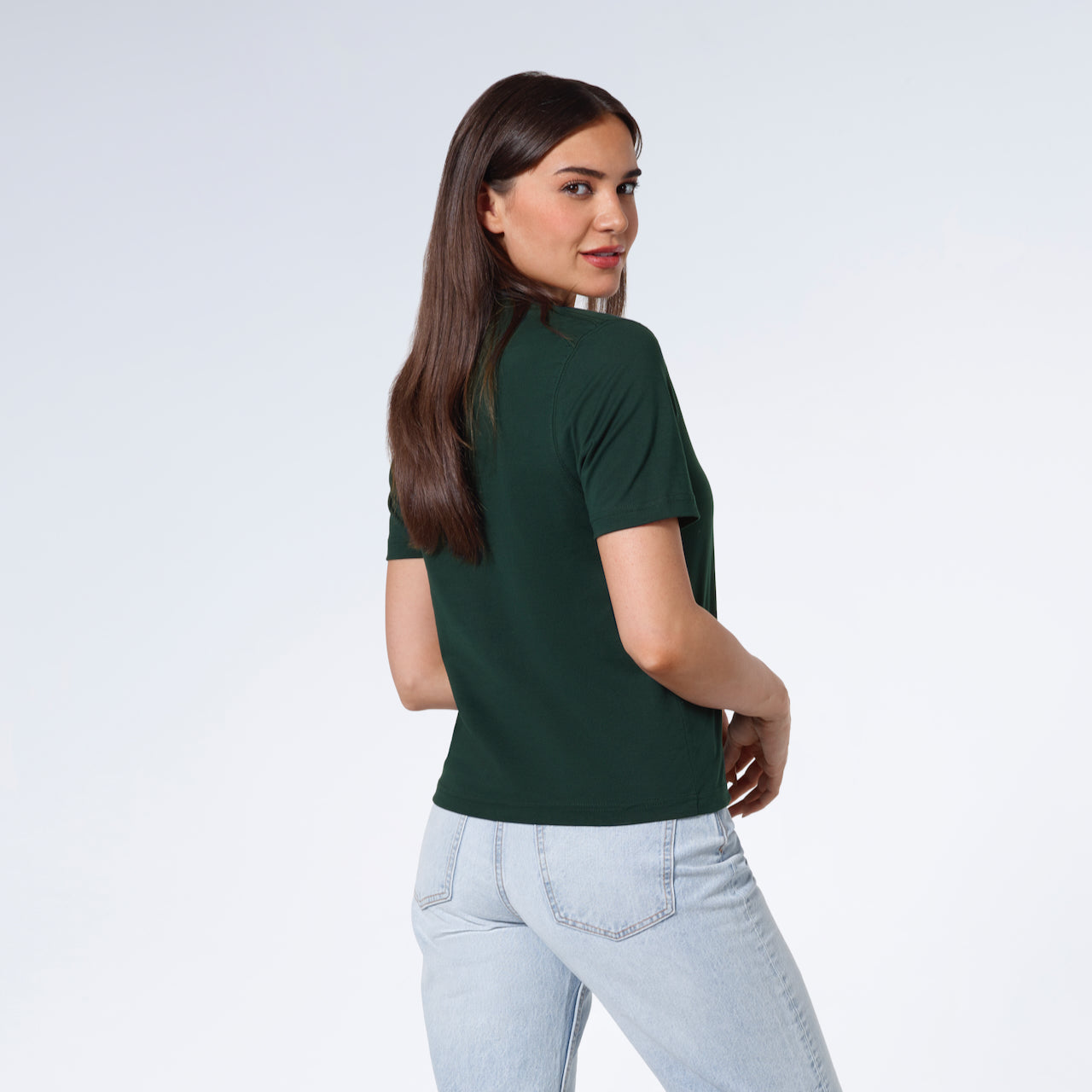 A woman turned towards the camera smiling, modelling a plain green short sleeve organic cotton t shirt.