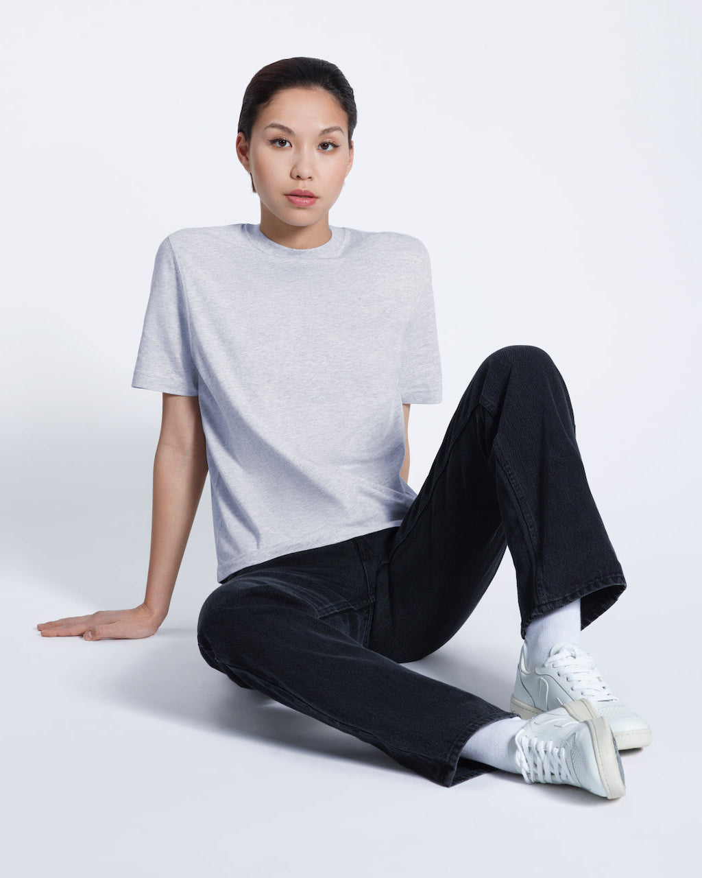 A woman sitting on the floor looking into the camera, modelling a plain grey short sleeve organic cotton t shirt.