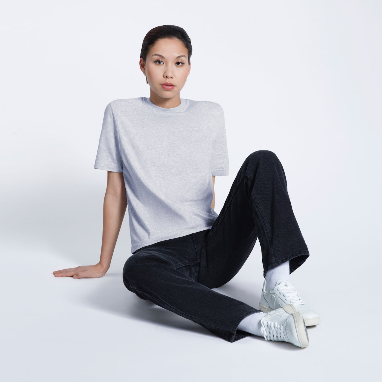 A woman sitting on the floor looking into the camera, modelling a plain grey short sleeve organic cotton t shirt.