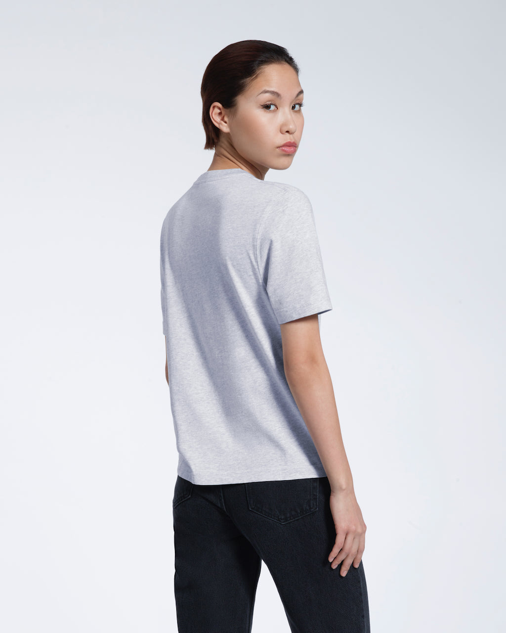 A woman turned towards the camera, modelling a plain grey short sleeve organic cotton t shirt.
