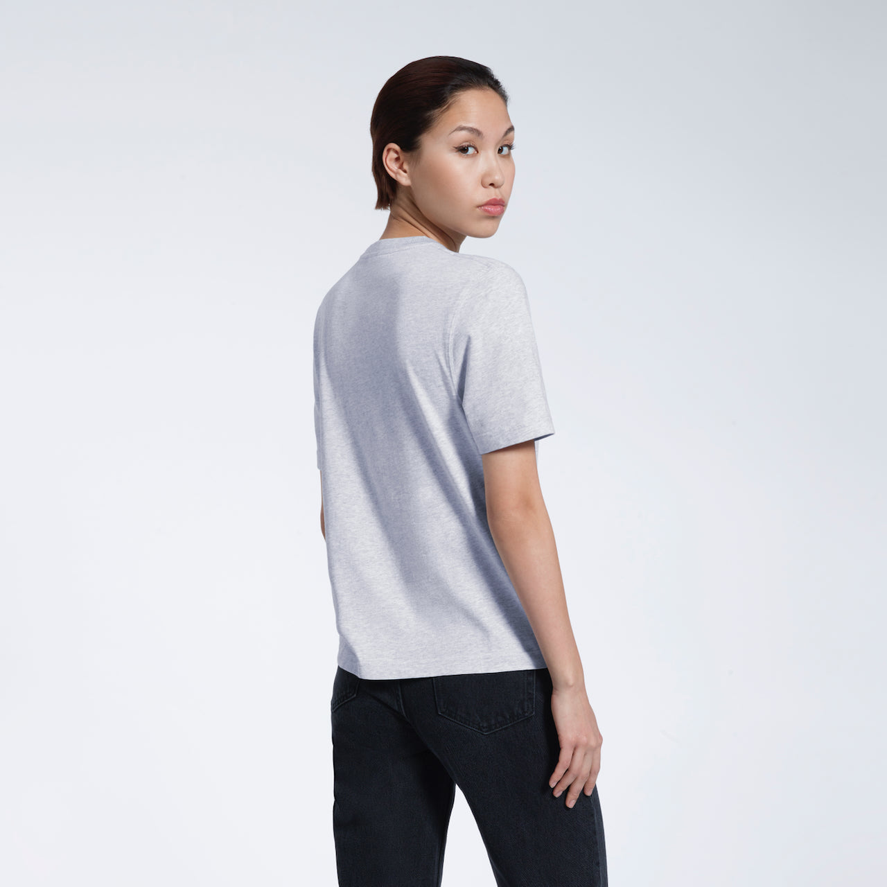 A woman turned towards the camera, modelling a plain grey short sleeve organic cotton t shirt.