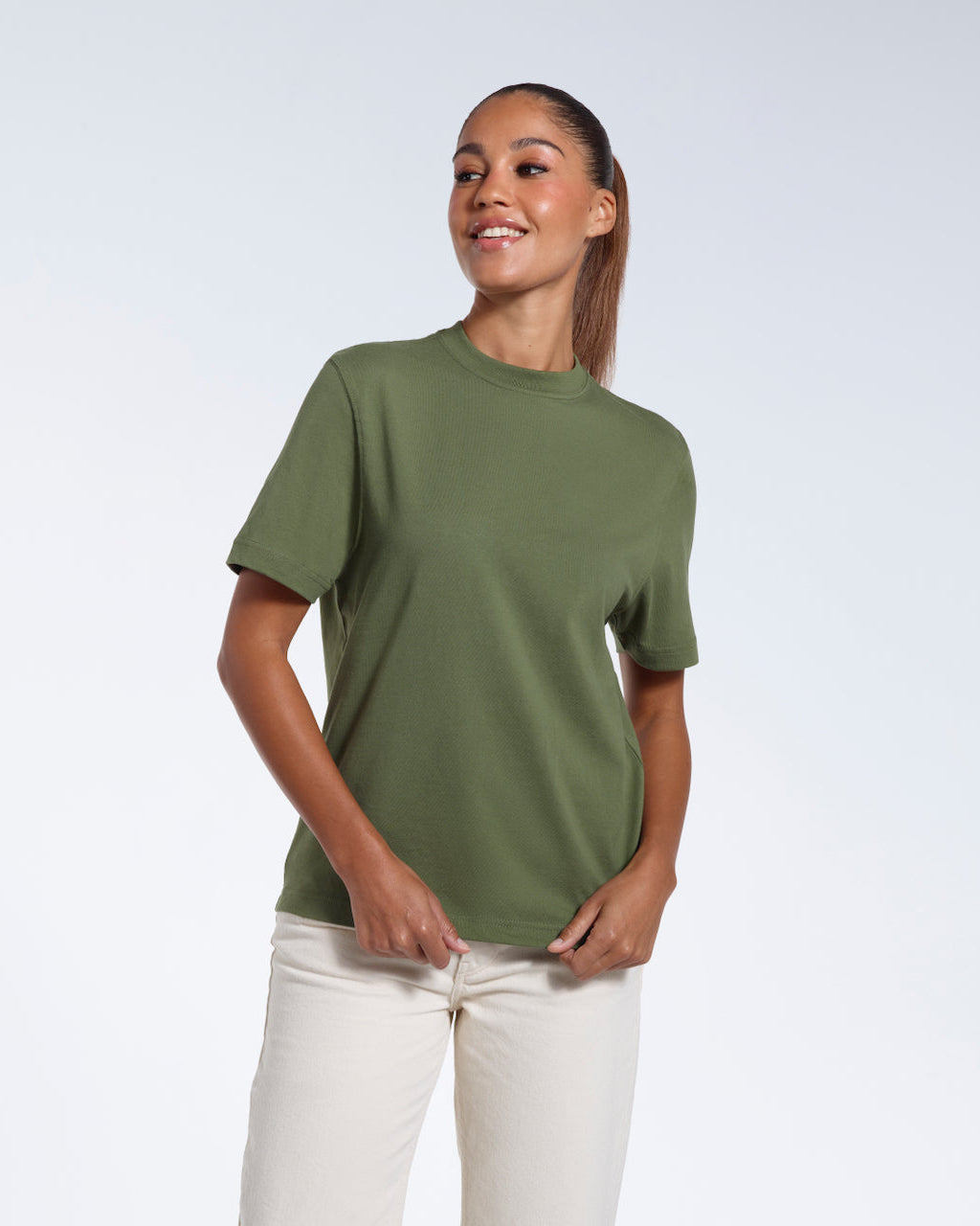 A woman smiling, touching the bottom of her plain khaki green short sleeve organic cotton t shirt.