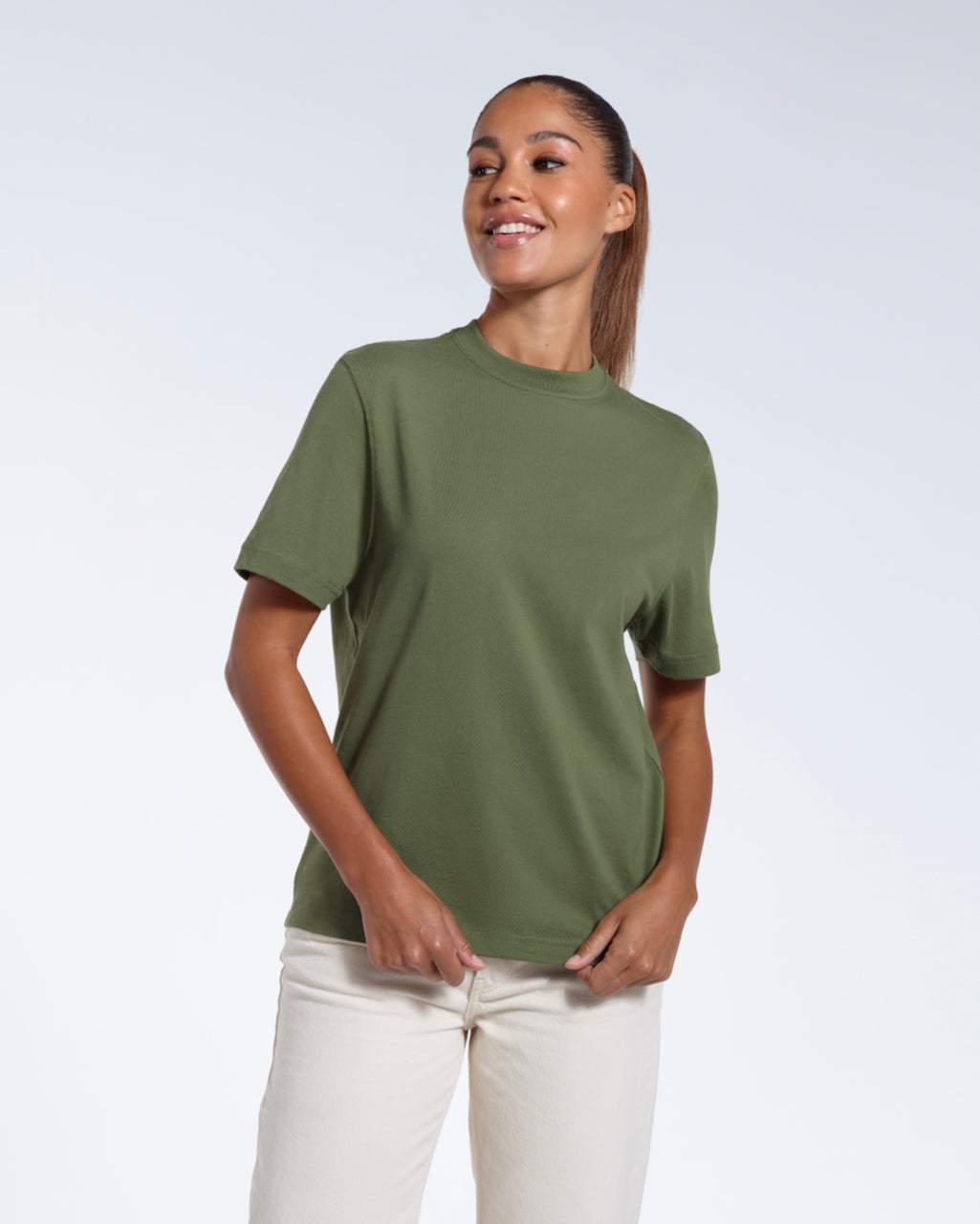 A woman smiling, touching the bottom of her plain khaki green short sleeve organic cotton t shirt.