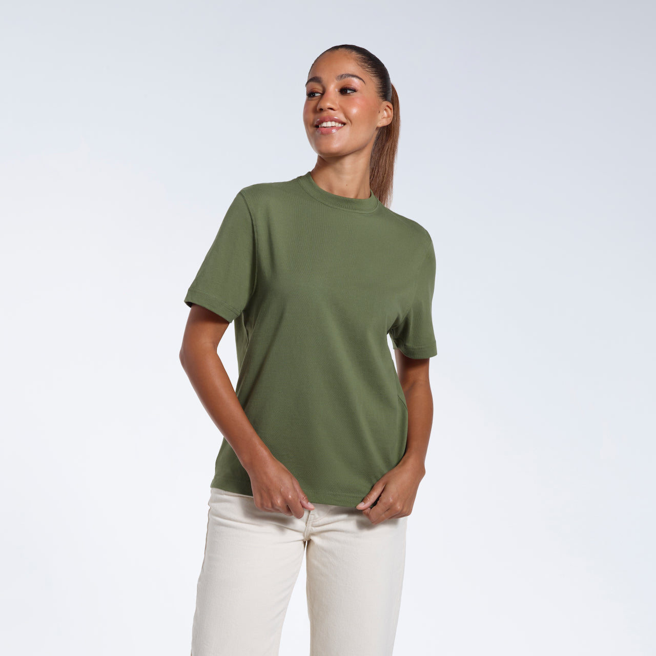 A woman smiling, touching the bottom of her plain khaki green short sleeve organic cotton t shirt.