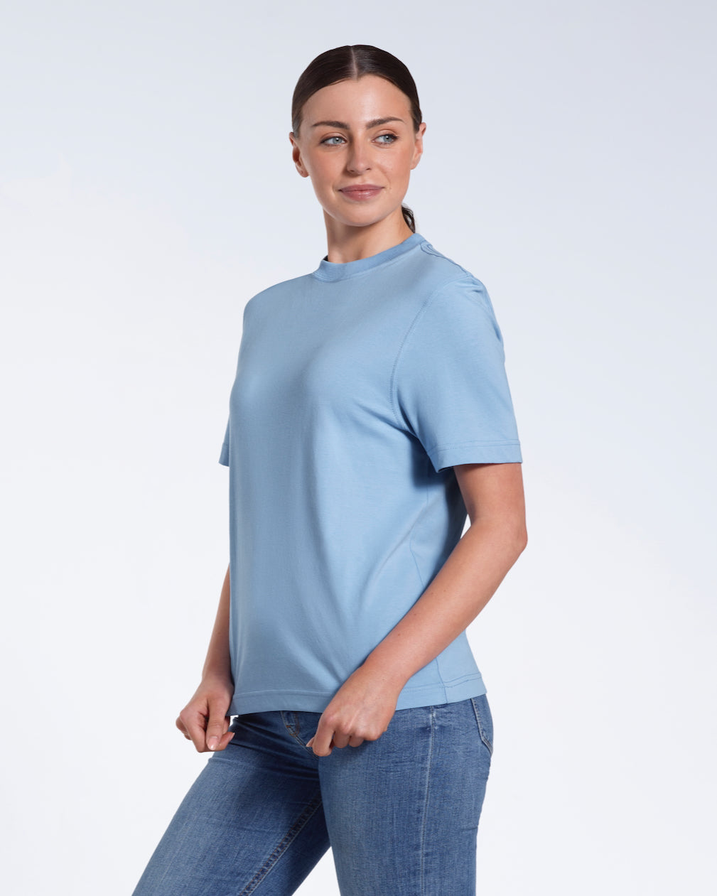 A woman smiling, touching the bottom of her plain blue short sleeve organic cotton t shirt.