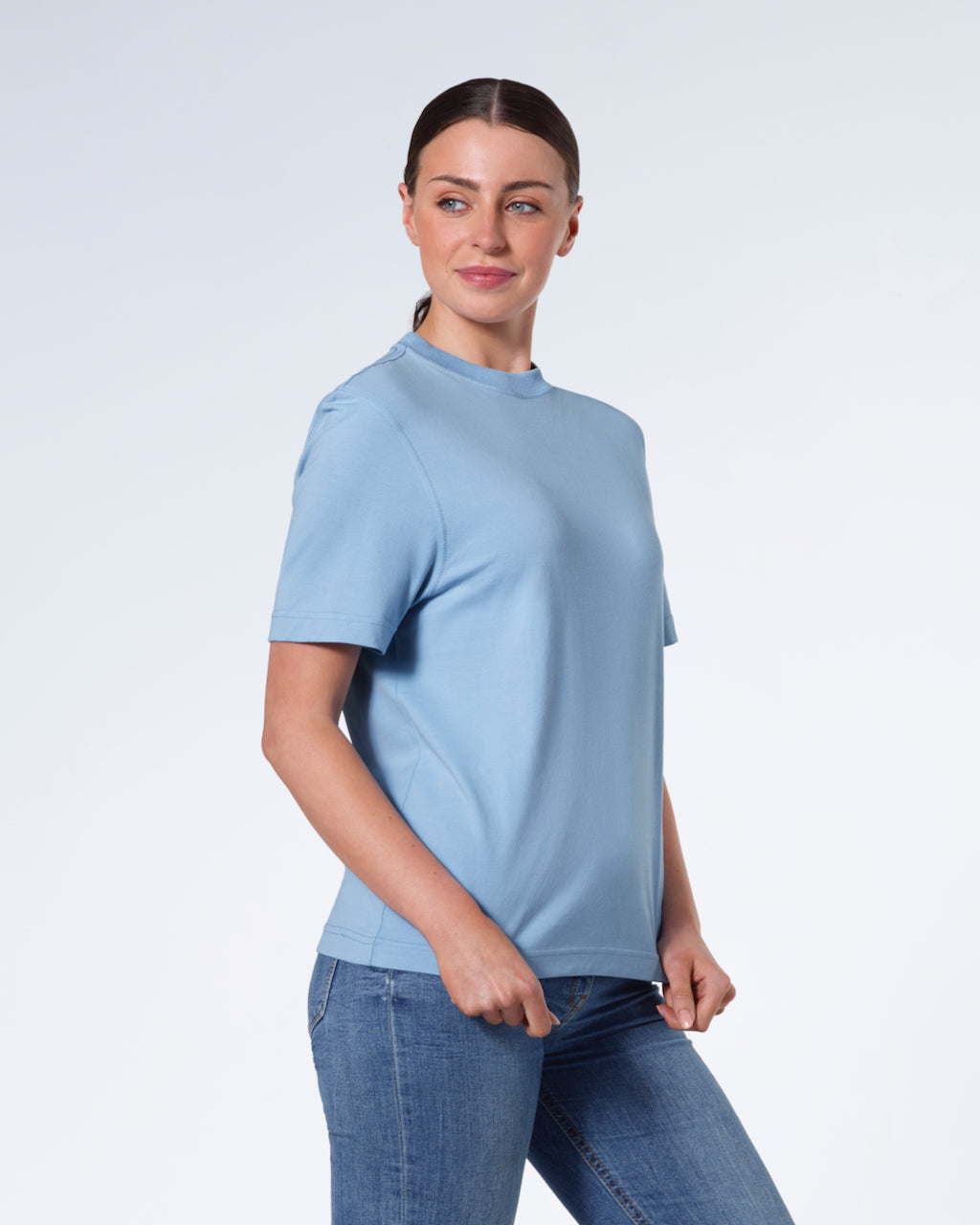 A woman smiling, touching the bottom of her plain blue short sleeve organic cotton t shirt.