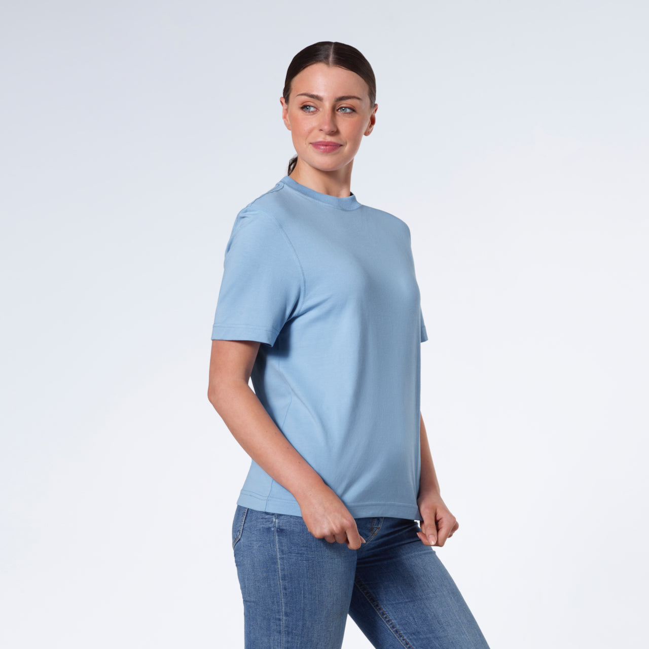 A woman smiling, touching the bottom of her plain blue short sleeve organic cotton t shirt.