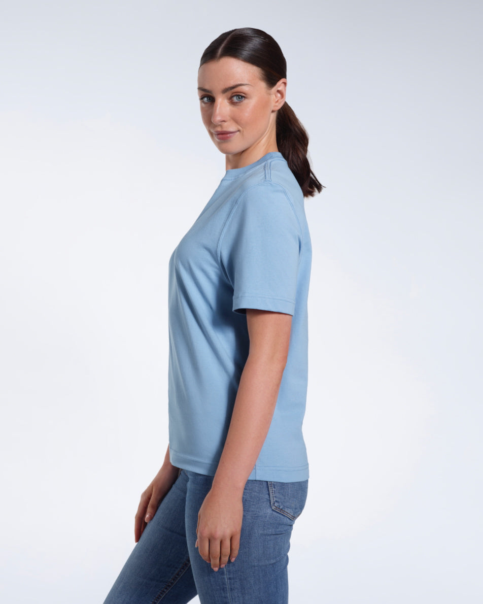 A woman facing side on and looking at the camera, modelling a plain blue short sleeve organic cotton t shirt.