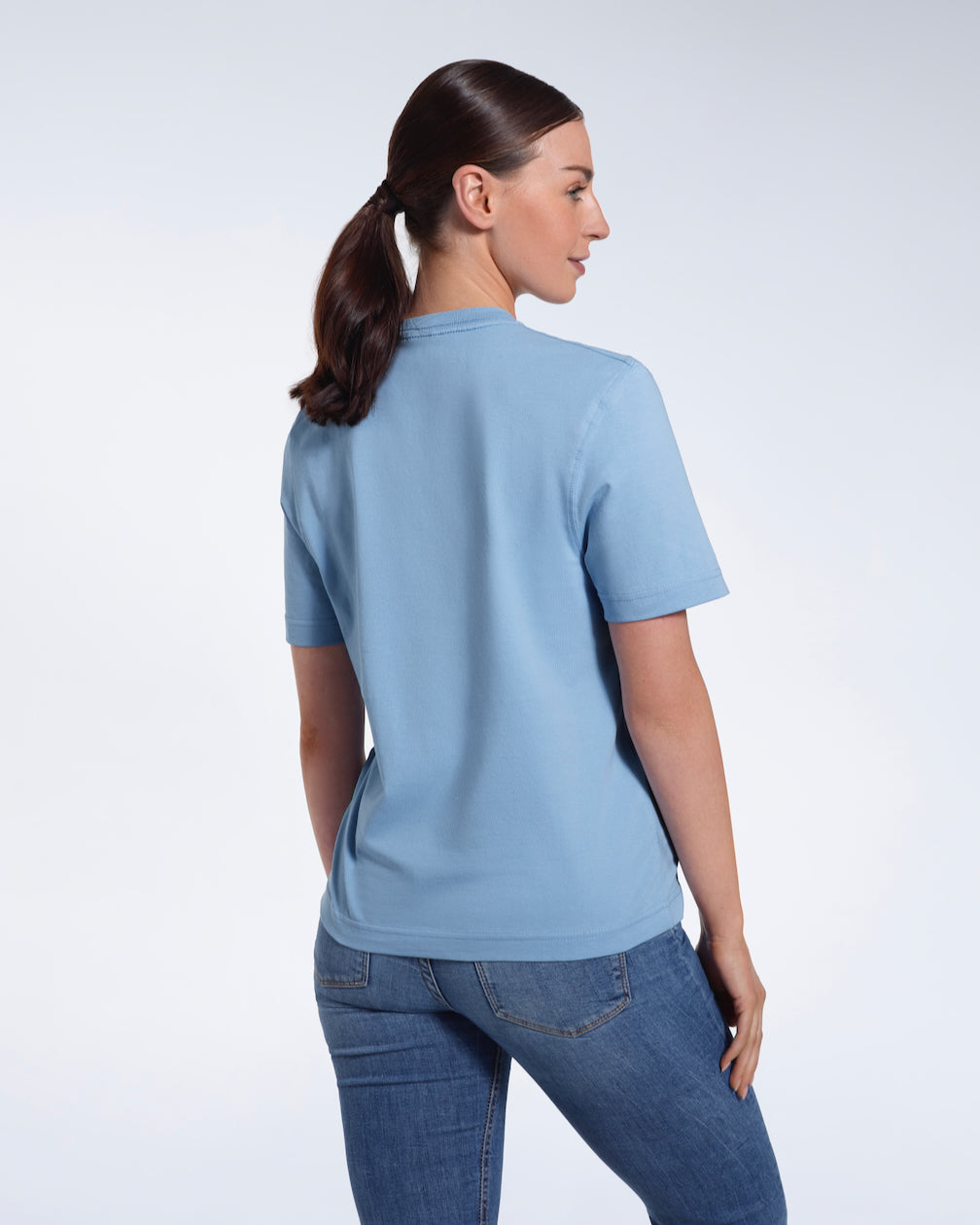 A woman with her back to the camera, modelling a plain blue short sleeve organic cotton t shirt.