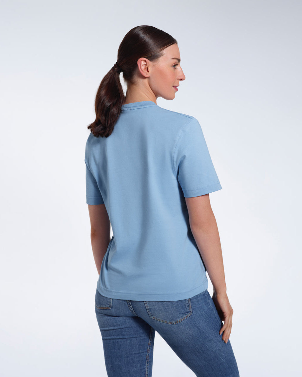 A woman with her back to the camera, modelling a plain blue short sleeve organic cotton t shirt.
