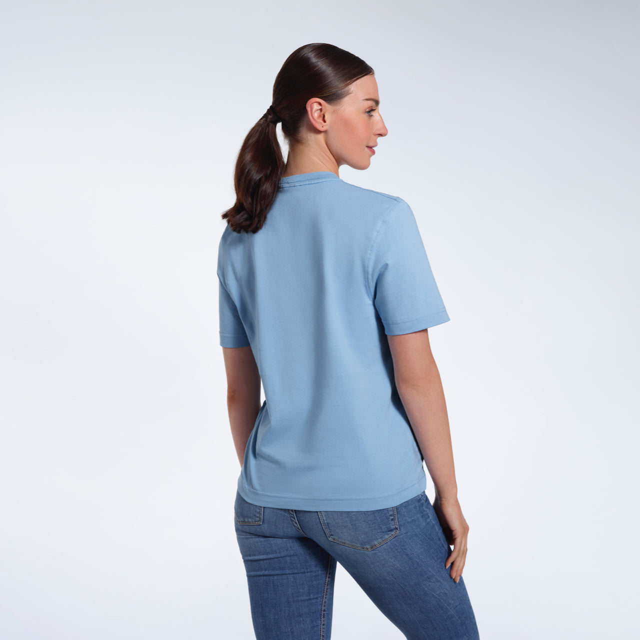 A woman with her back to the camera, modelling a plain blue short sleeve organic cotton t shirt.