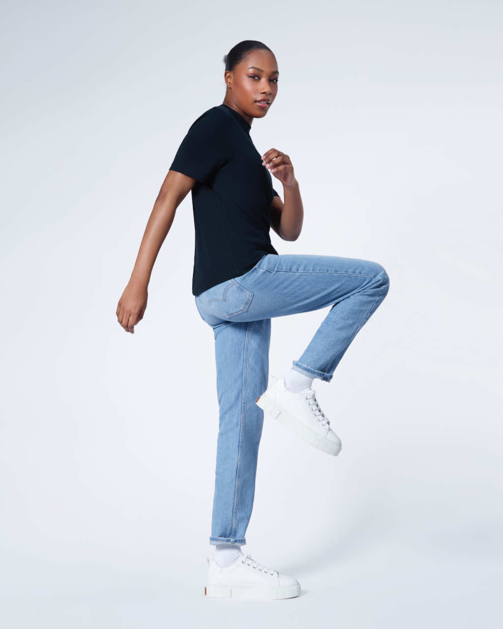 A woman turning with one leg bent looking at the camera, modelling a plain navy short sleeve organic cotton t shirt.