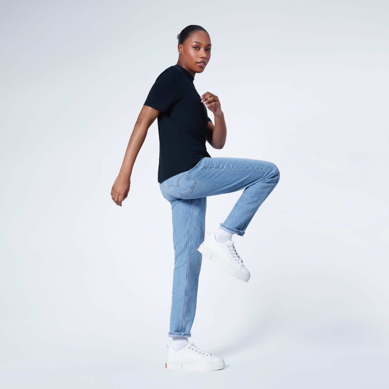 A woman turning with one leg bent looking at the camera, modelling a plain navy short sleeve organic cotton t shirt.