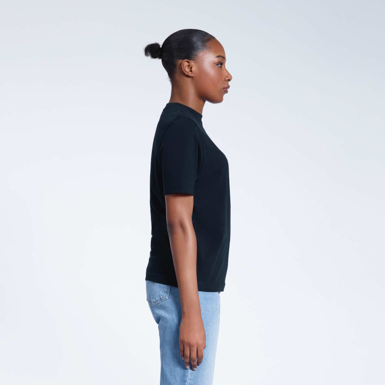 A woman facing side on, modelling a plain navy short sleeve organic cotton t shirt.