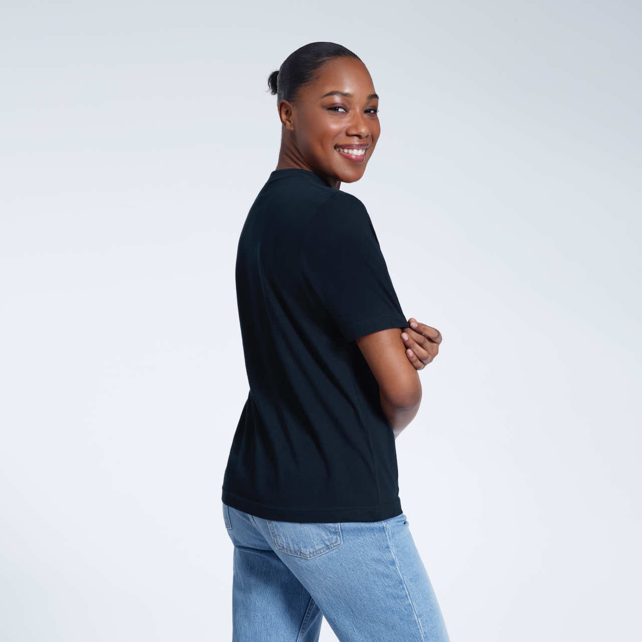 A woman turned towards the camera touching her sleeve smiling, modelling a plain navy short sleeve organic cotton t shirt.