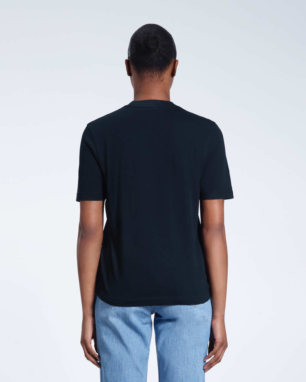 A woman with her back to the camera, modelling a plain navy short sleeve organic cotton t shirt.