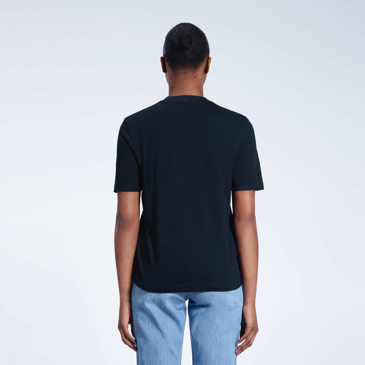 A woman with her back to the camera, modelling a plain navy short sleeve organic cotton t shirt.
