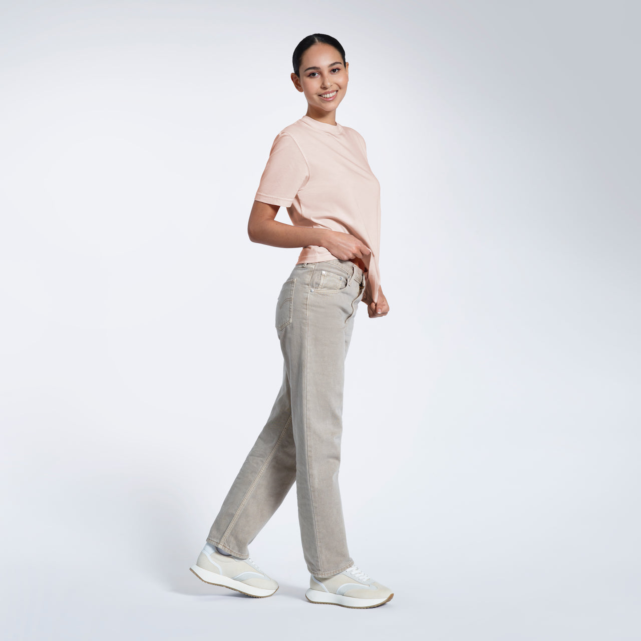 A woman walking and smiling at the camera, modelling a plain pink short sleeve organic cotton t shirt.