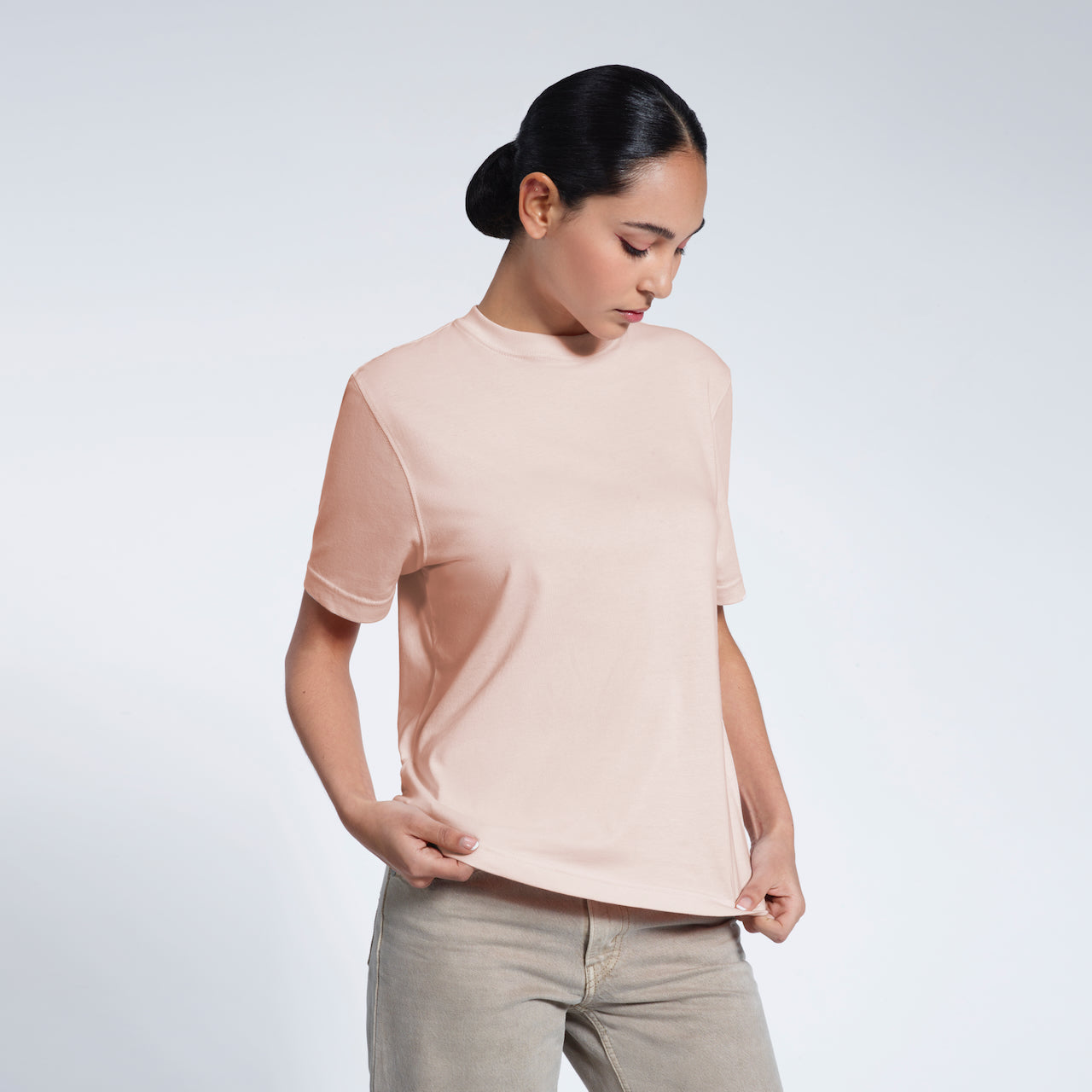 A woman looking down and touching the bottom of her plain pink short sleeve organic cotton t shirt.